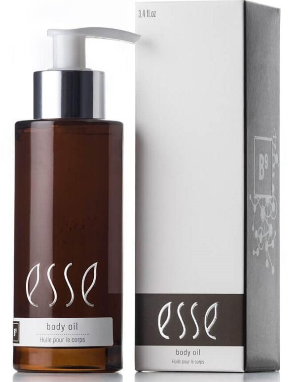 A bottle of Esse Body Oil, presented in a brown, transparent vessel equipped with a pump dispenser, positioned adjacent to its matching white and gray packaging box. The label on both the bottle and the box prominently displays the text "Esse Body Oil" and "Huile pour le corps.
