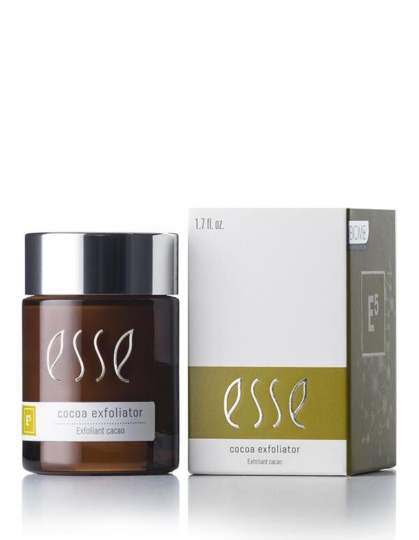 A brown container of Esse Cocoa Exfoliator, featuring a black lid and white text, is placed next to its product box. The box is white with green detailing and matching white text, displaying the same information as the container.