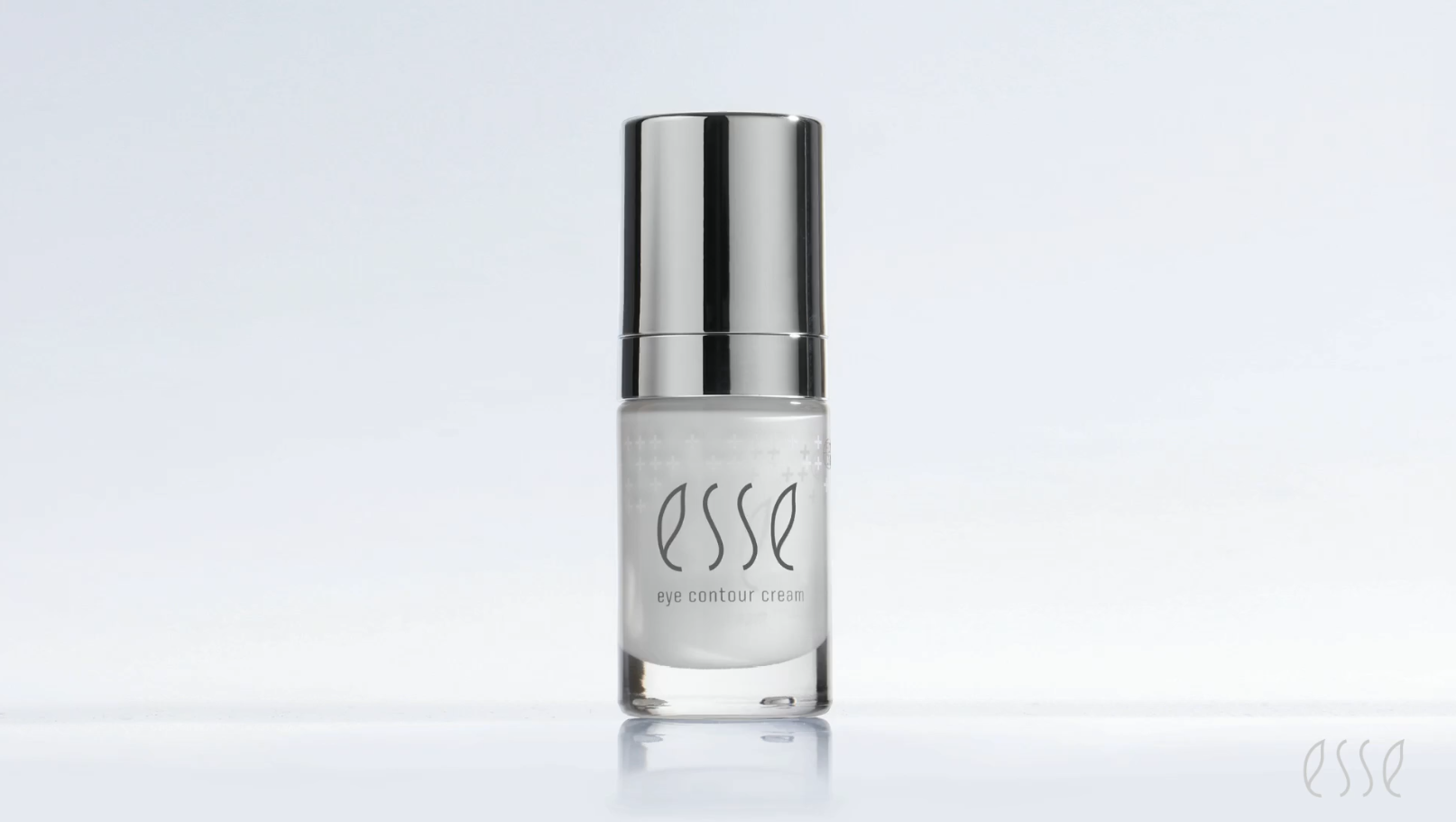 A small bottle of the Esse Eye Contour Cream stands upright on a reflective surface. The bottle features a silver cap and a clear body, allowing the product inside to be visible. The word "Esse" is elegantly written on the bottle, with "Eye Contour Cream" noted below.