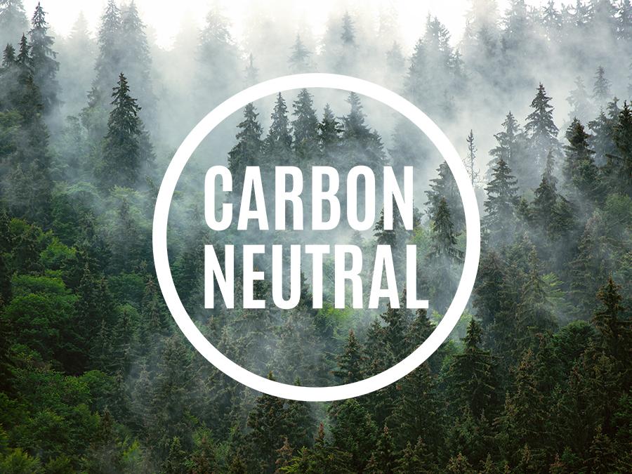 A misty forest filled with dense evergreen trees. The text "CARBON NEUTRAL" is prominently displayed in bold white letters within a white circular border overlaying the center of the image.
