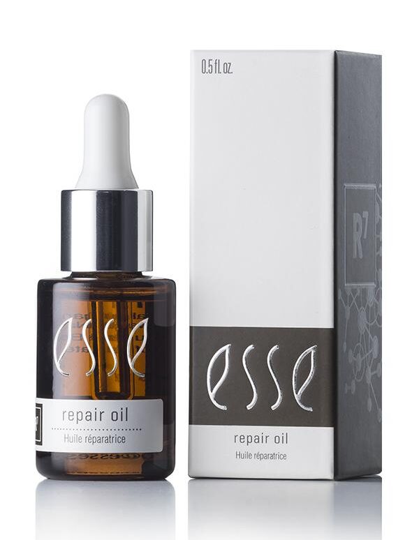 A brown glass dropper bottle of Esse Repair Oil stands next to its corresponding white and gray box packaging. The label on both the bottle and the box reads "Esse Repair Oil - Huile réparatrice." The bottle has a silver cap and a white dropper.