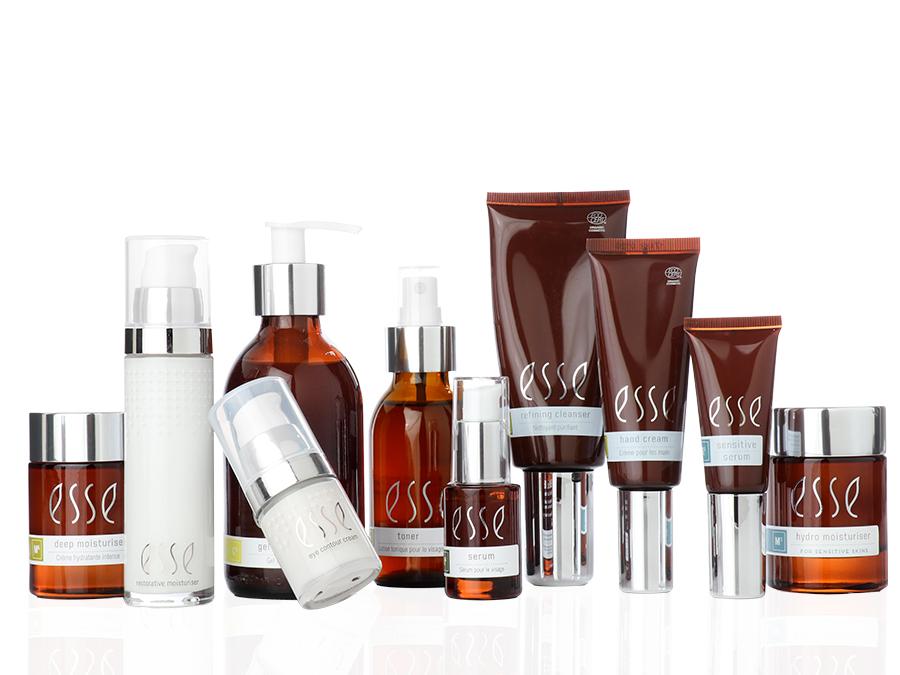 A group of skincare products in brown and clear glass containers with silver caps. The products include moisturizers, serums, and cleansers, all labeled with "esse." Some bottles have pumps, while others have caps, creating a clean and organized display.