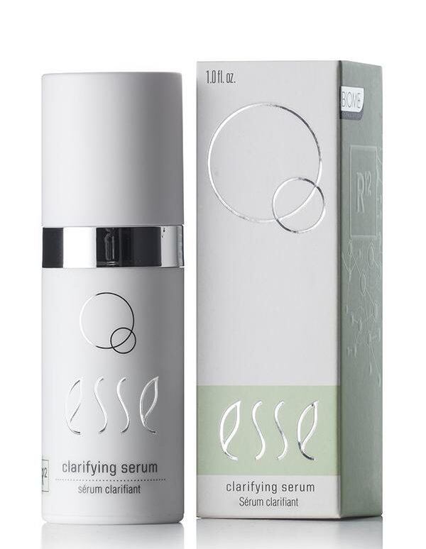 A 1.01 fl. oz. bottle of Esse Clarifying Serum is displayed alongside its packaging. The bottle, which is white with a silver cap, bears a label adorned with elegant circular designs. The packaging mirrors the design of the bottle and includes additional informational text.