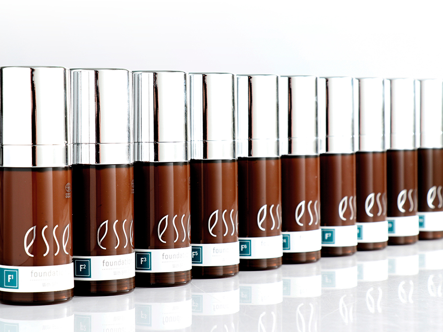A row of identical brown bottles with shiny silver caps and "esse" branding is lined up in front of a white background. Each bottle is labeled "foundation" at the bottom with an "F3" marking above the label.