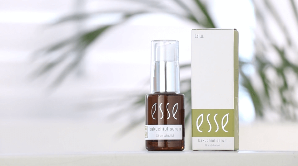 A small bottle of Esse Bakuchiol Serum is displayed next to its matching rectangular packaging. The bottle is dark brown with a white label, and the packaging is primarily white and green. The background is softly blurred, giving a clean and minimalistic feel.